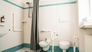 Une salle de bain équipée d’un bidet, de toilettes, d’une douche et d’un porte-serviettes.