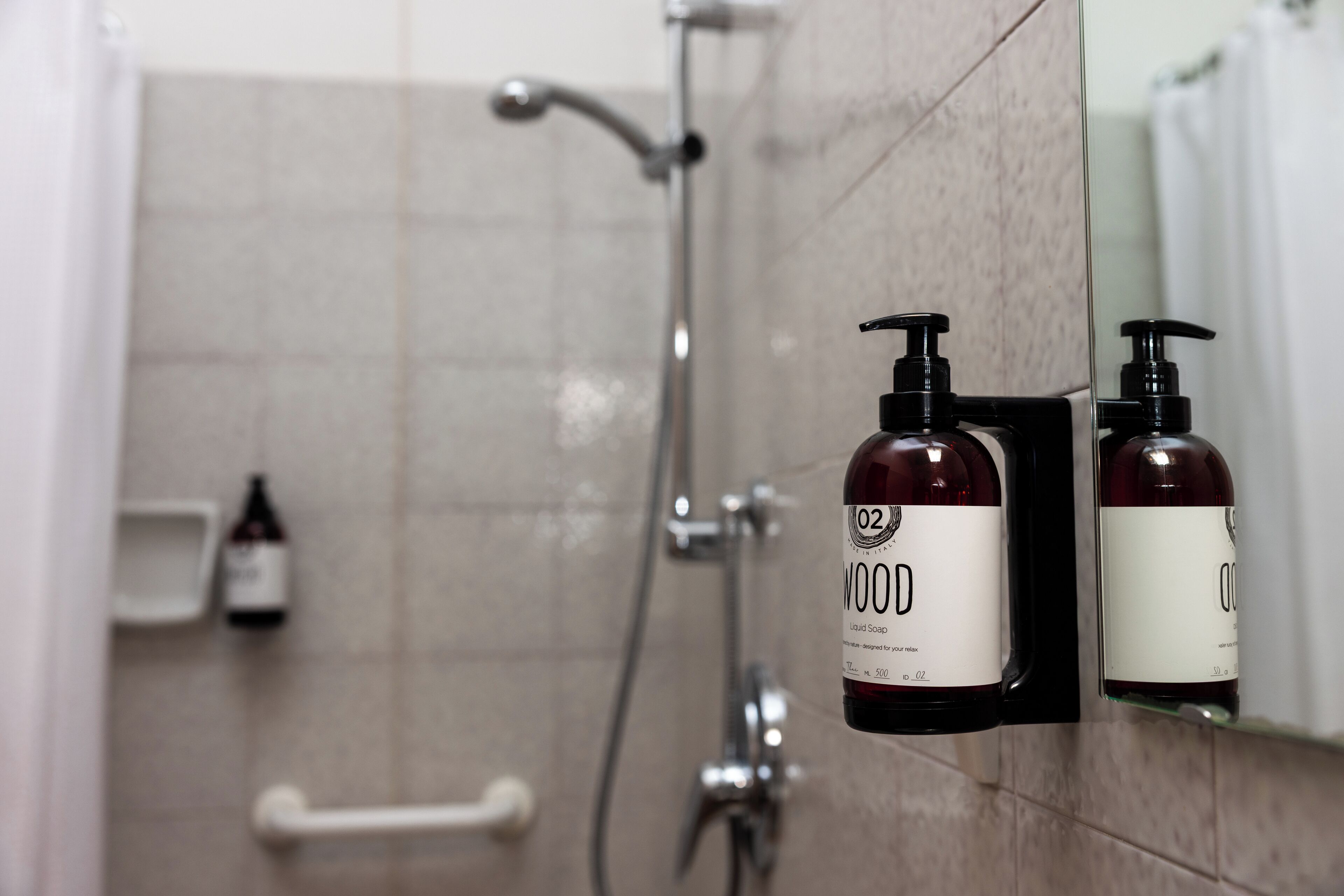 A bathroom with a shower, a hand dryer, and two bottles of liquid soap on a wall-mounted soap dispenser.