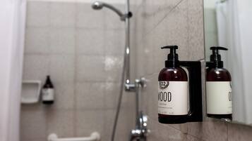 A bathroom with a shower, a hand dryer, and two bottles of liquid soap on a wall-mounted soap dispenser.