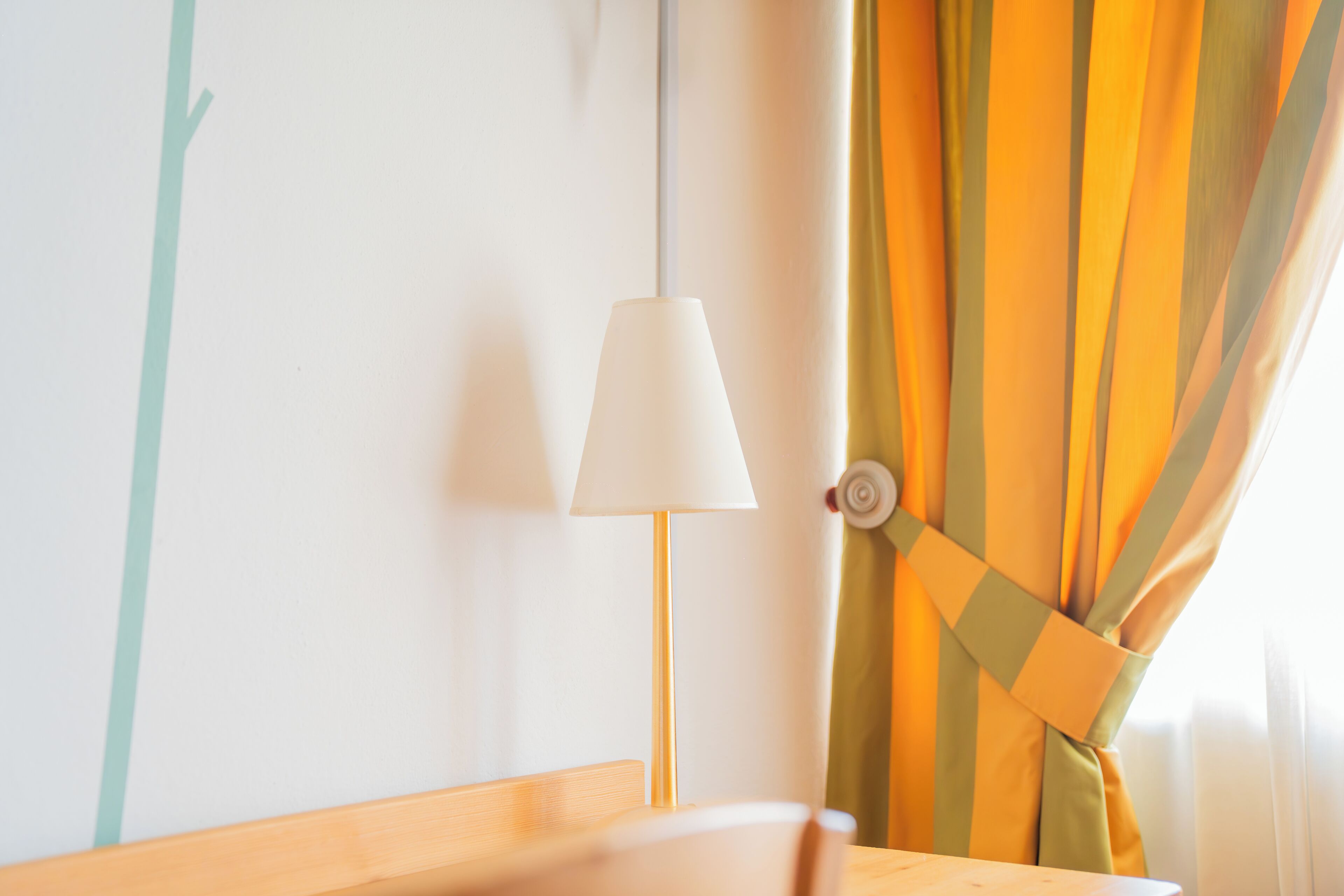 Ein Zimmer mit hölzernem Kopfteil, einer weißen Wand, einer weißen Lampe und einem Fenster mit gelb-grünen Streifen.