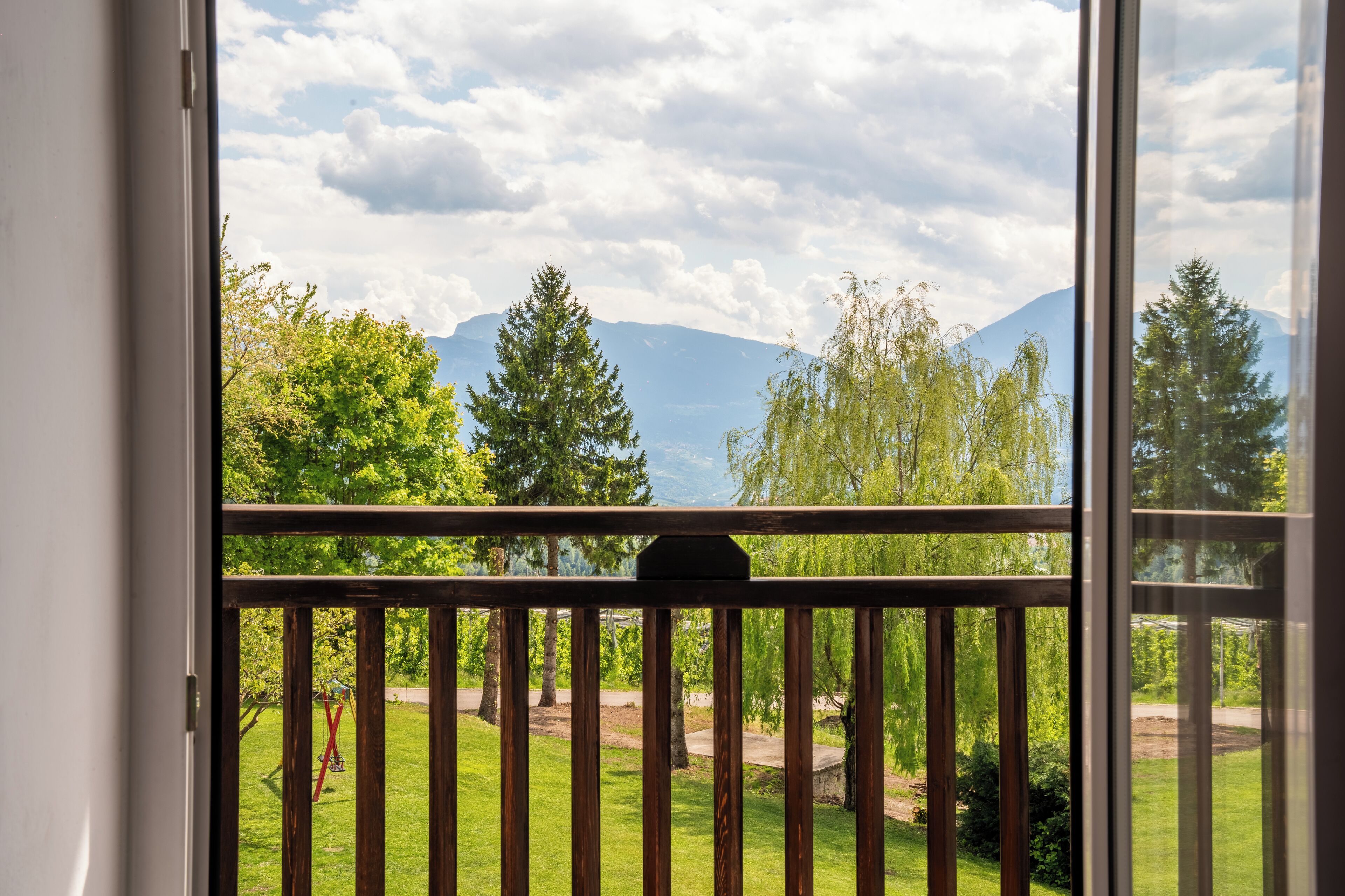 A balcony with a view of a grassy yard, trees, and mountains in the distance.