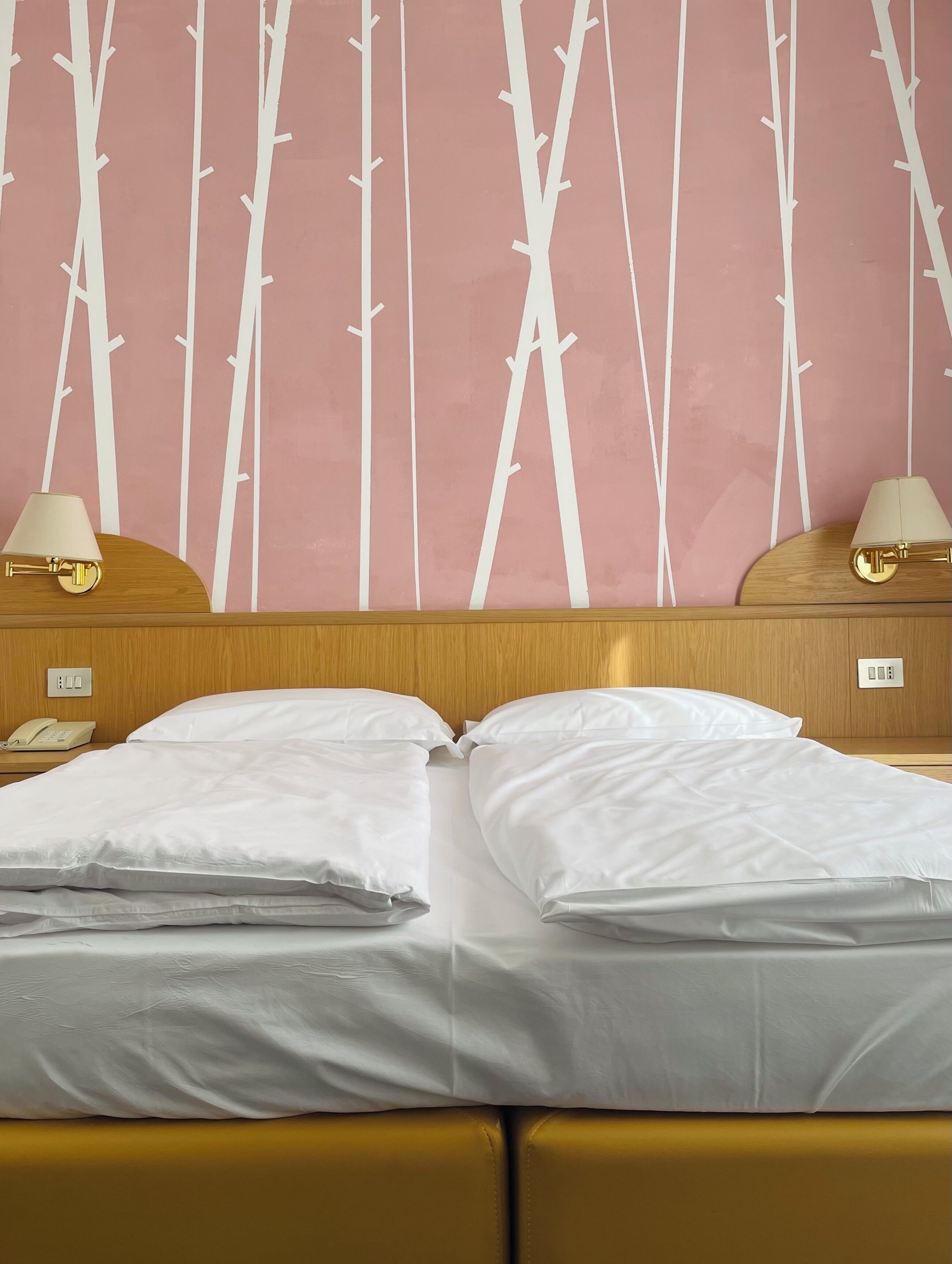 Habitación de hotel con cama, dos lámparas de noche, cabecera de madera y pared con diseño de bambú.