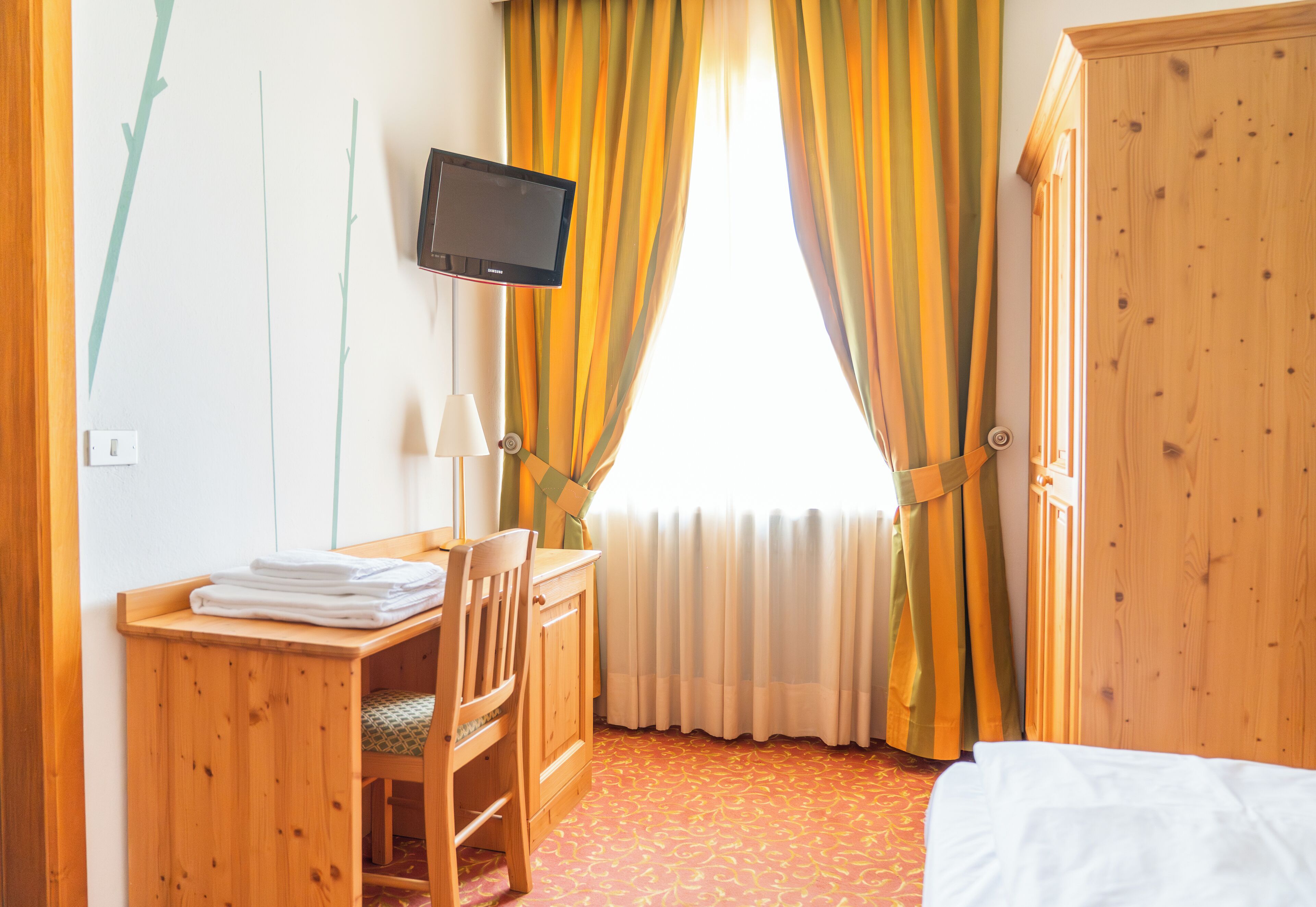 Habitación de hotel con escritorio de madera, una silla, televisor montado en la pared, cama y armario.