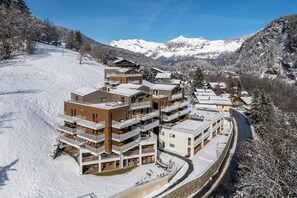 A modern ski resort building with multiple balconies, surrounded by snow-covered mountains and a clear sky. - Camox – Charming Apartment in Les Houches (Les Houches)
