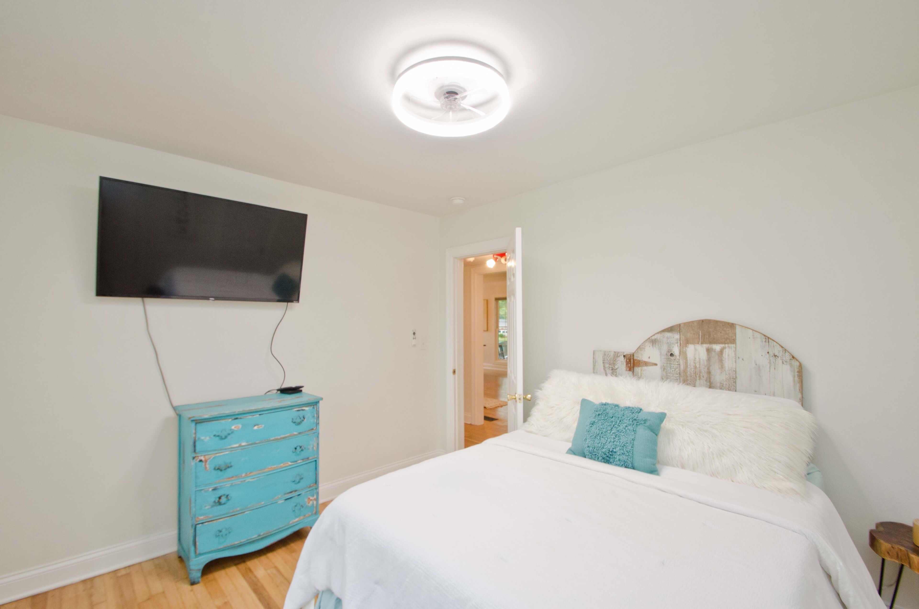 A bedroom with a bed, a television mounted on the wall, and a blue dresser.