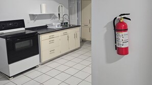 A kitchen with a stove, sink, and cabinets, a fire extinguisher mounted on the wall, and a tiled floor.