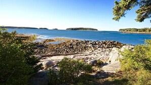 A rocky shoreline with calm water, distant islands, and dense greenery. - Pumpkin Point, 5BR Ocean Views, Dock (St George)