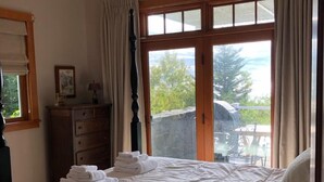 A bedroom with a bed, a dresser, a window with curtains, and a view of the outdoors. - Pumpkin Point, 5BR Ocean Views, Dock (St George)