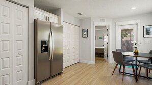 Eine moderne Küche mit Edelstahlkühlschrank, weißen Schränken und einem Essbereich mit Tisch und Stühlen.