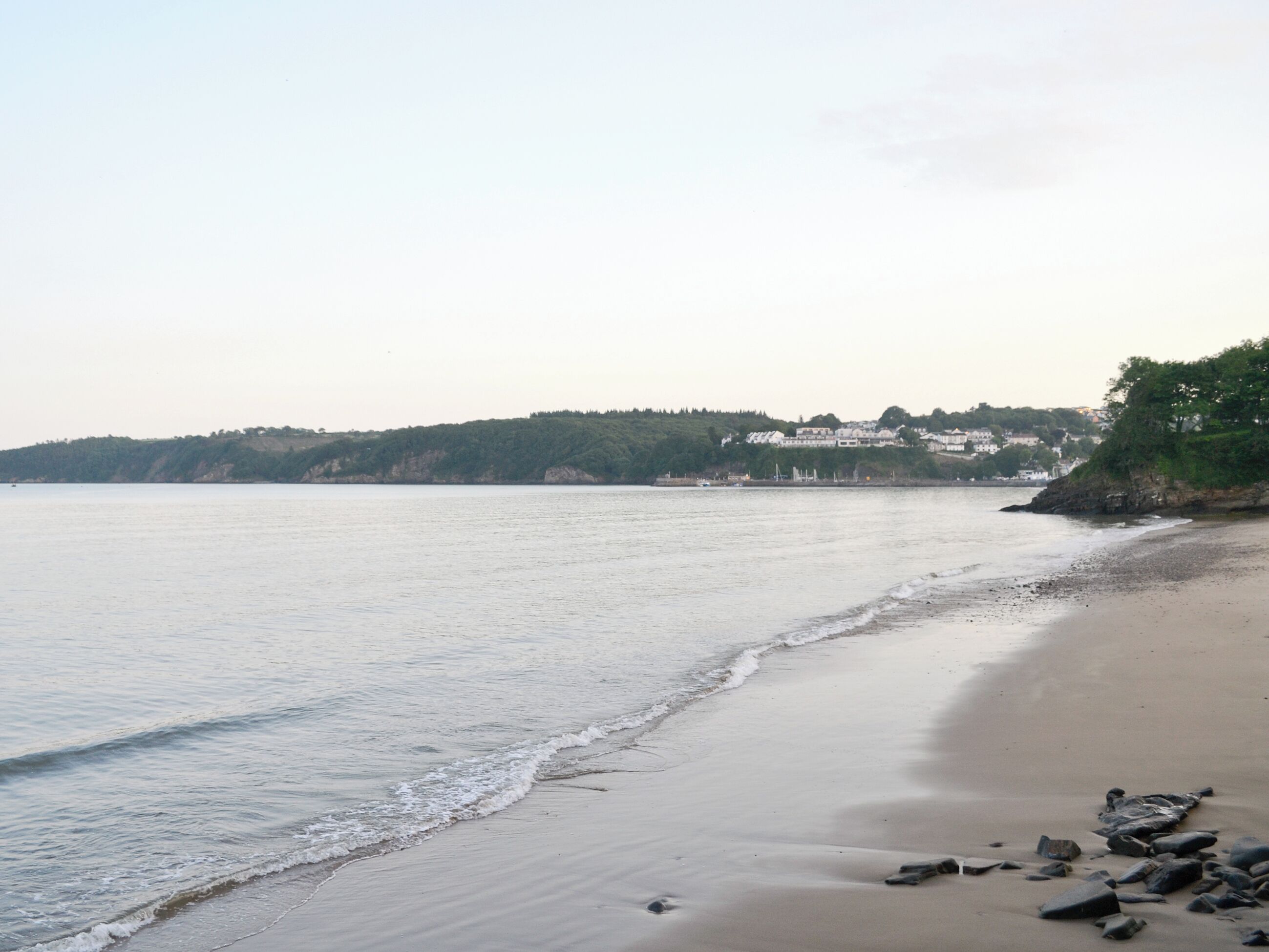 A beach with calm waters, a sandy shore, and buildings in the background.