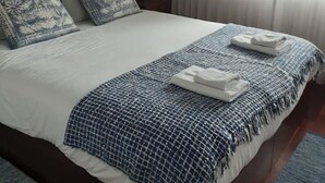 Un letto rifatto con cura, una coperta a quadretti blu e bianchi, due cuscini decorati e asciugamani piegati su un lato.