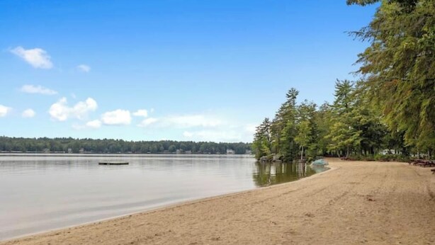 Une plage de sable fin, avec un lac paisible et des arbres en arrière-plan.