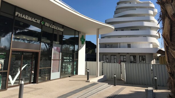 Un bâtiment moderne, avec une enseigne de pharmacie, une entrée incurvée et une structure à plusieurs niveaux dotée de balcons.
