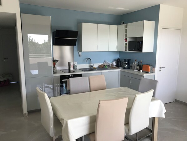 A modern kitchen with white cabinets, a black microwave, and a dining area with a table and chairs.
