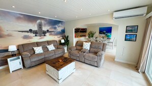 Un salon spacieux avec deux canapés gris, une table basse en bois et une grande fresque représentant un avion sur le mur.
