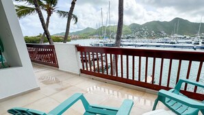 Un balcon offrant une vue sur un port de plaisance, des palmiers et un paysage montagneux en arrière-plan.