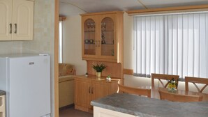 Ett kompakt kök med ett kylskåp, träskåp, ett matbord med stolar och ett fönster med persienner.