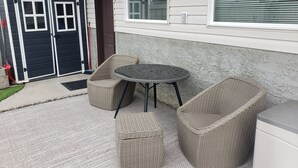 A patio with wicker furniture, a small round table, and a door to a garage. - Walkout Garden 1-bedroom  in Grande Prairie AC, WiFi, laundry, parking space (Grande Prairie)