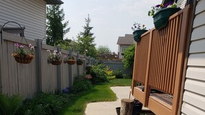 A narrow concrete pathway flanked by a wooden fence and a wooden deck. - Walkout Garden 1-bedroom  in Grande Prairie AC, WiFi, laundry, parking space (Grande Prairie)