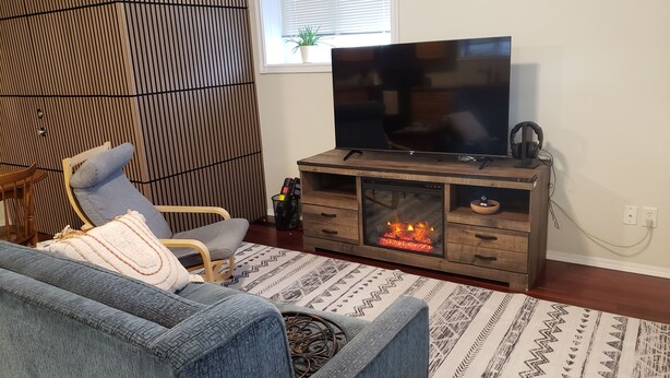 A living room with a sofa, a TV, a fireplace, and a window with blinds. - Walkout Garden 1-bedroom  in Grande Prairie AC, WiFi, laundry, parking space (Grande Prairie)