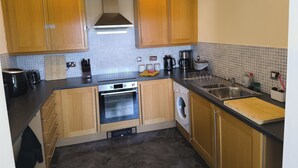 A kitchen with wooden cabinets, a built-in oven, a washing machine, and a coffee maker. - Cardiff Apt - Sleeps 6 - Castle & Stadium Nearby (Cardiff)