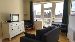 A living room with a sofa, a TV on a dresser, a chair, and a dining table with chairs. - Cardiff Apt - Sleeps 6 - Castle & Stadium Nearby (Cardiff)