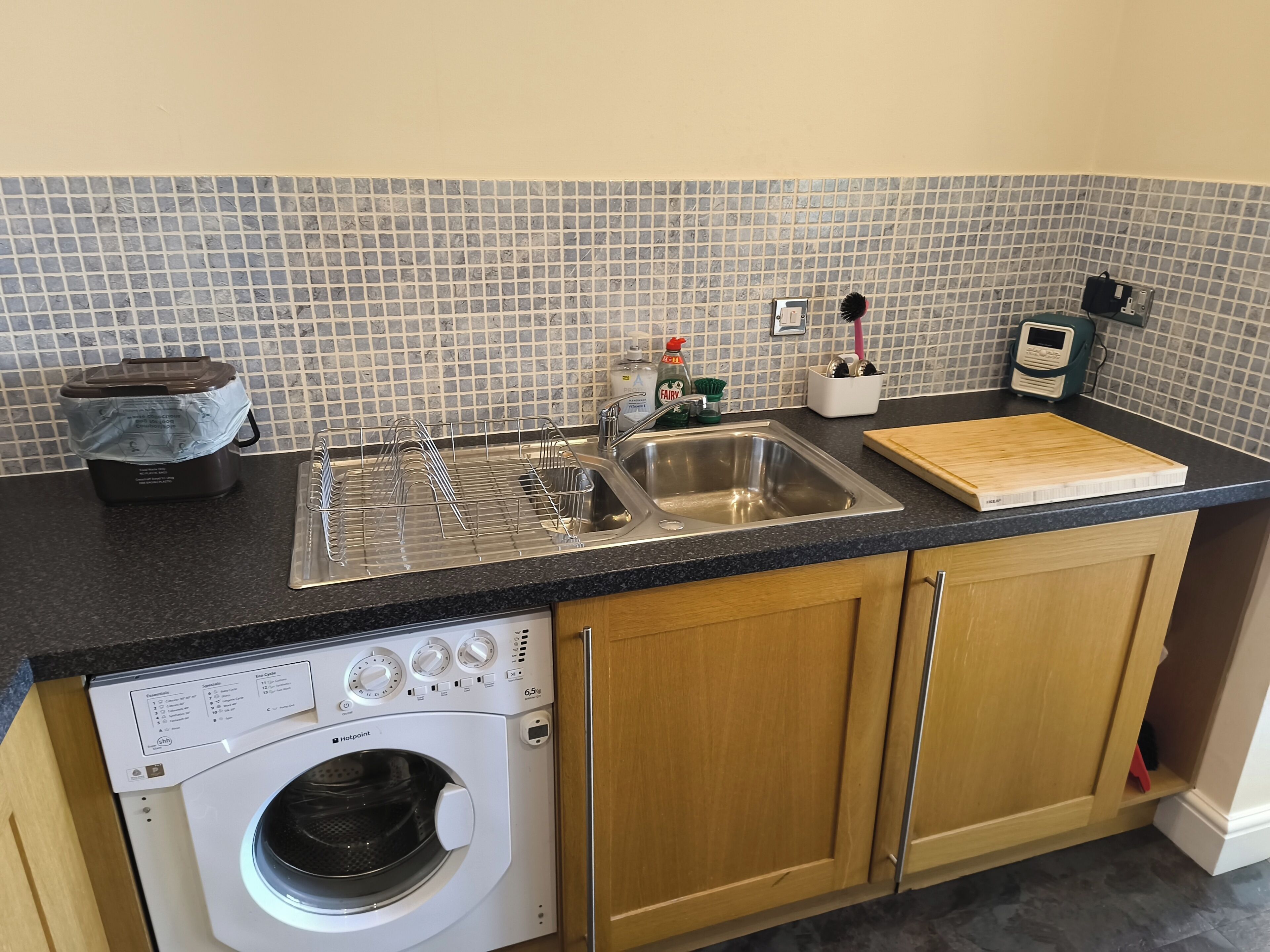 A kitchen with a built-in washing machine, a sink, and a cutting board on the countertop.