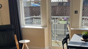 A room with a large window, a small round table, a black chair, and a dining table with chairs. - Cardiff Apt - Sleeps 6 - Castle & Stadium Nearby (Cardiff)