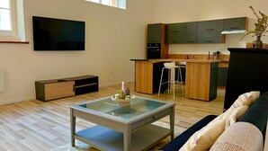 Una sala de estar moderna con una mesa de centro de vidrio, un sofá y una cocina con armarios de madera y un taburete de bar.