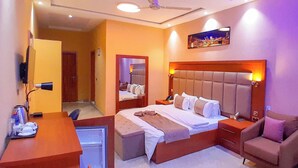 A hotel room with a large bed, a desk with a chair, a sofa, and a television. - Heartland Hotel  (Ada)