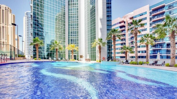 Une piscine bordée de palmiers, avec des bâtiments modernes en arrière-plan.