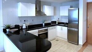 Une cuisine moderne avec des meubles blancs, un plan de travail noir, un réfrigérateur en acier inoxydable et un four à micro-ondes.