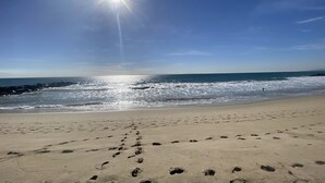 A beach with footprints leading to the water, a clear sky, and the sun shining.