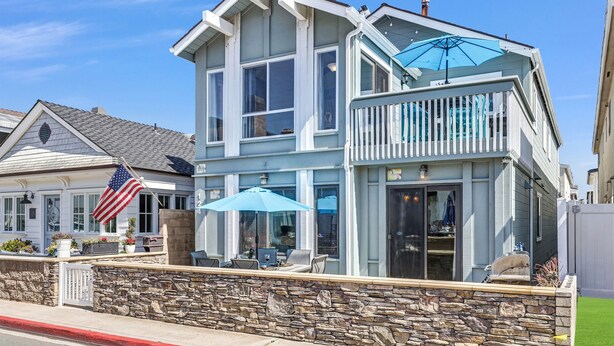 A two-story house with a balcony, stone wall, and American flag.