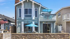 A two-story house with a stone foundation, a balcony with a blue umbrella, and an American flag.
