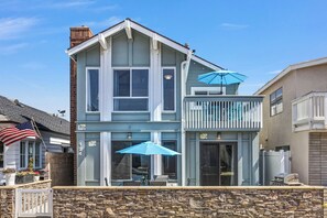 Ein zweistöckiges Haus mit Steinunterbau, einem Balkon mit blauem Sonnenschirm und einer amerikanischen Flagge.