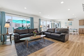 A spacious living room with two leather sofas, a coffee table, and a dining area with a table and chairs.