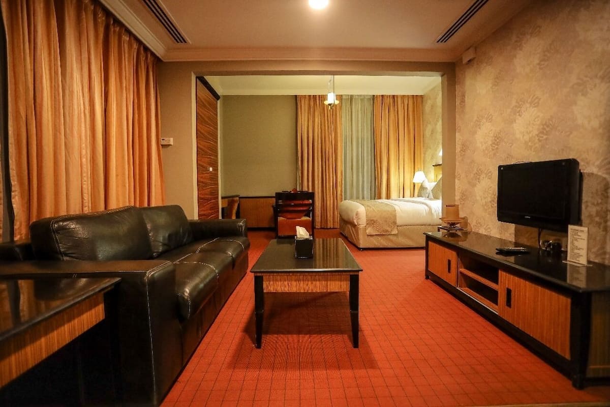 A hotel room with a leather sofa, a small table, a bed with white linens, a television, and a red carpeted floor.