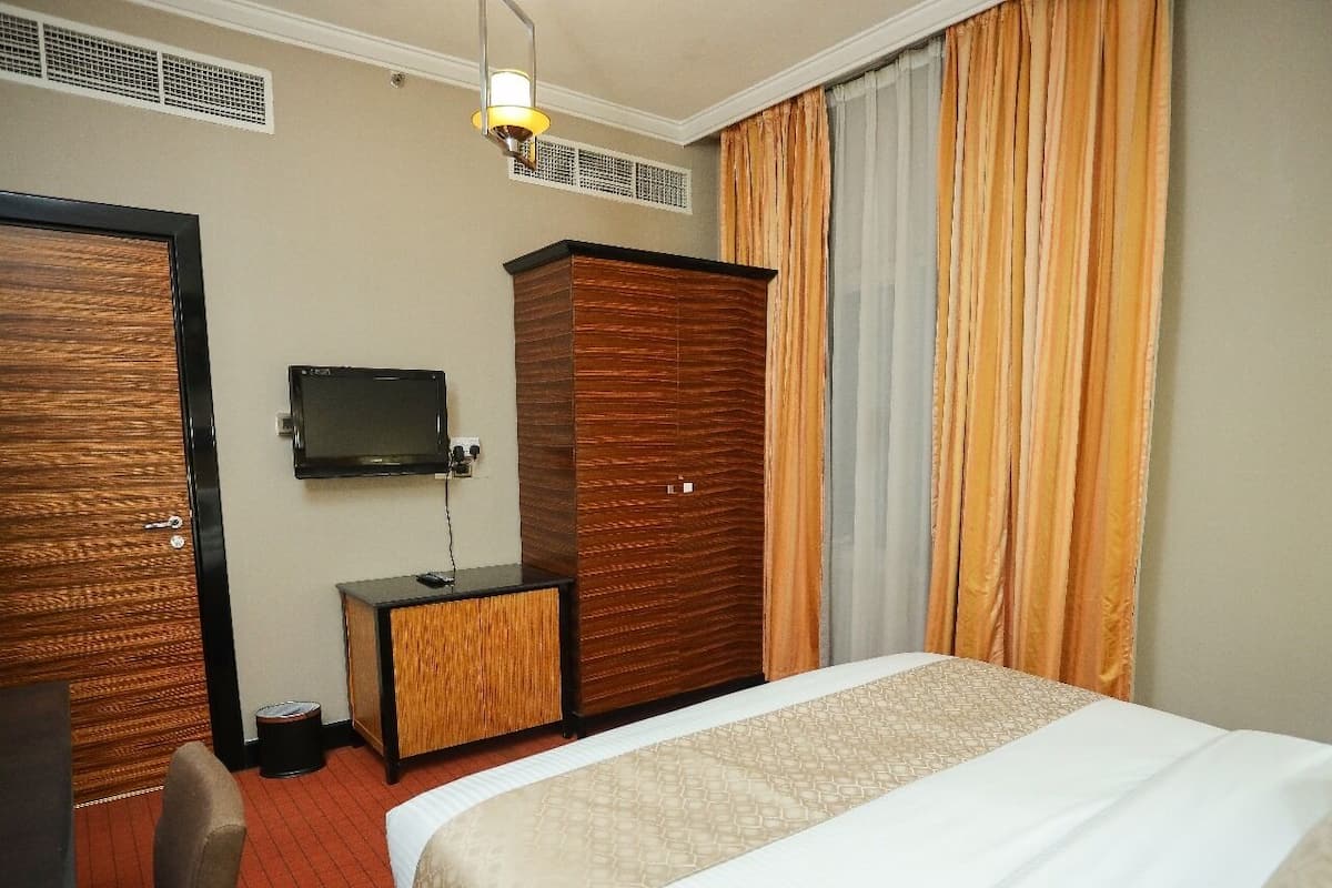 A hotel room with a bed, a TV, a wooden wardrobe, and a desk.