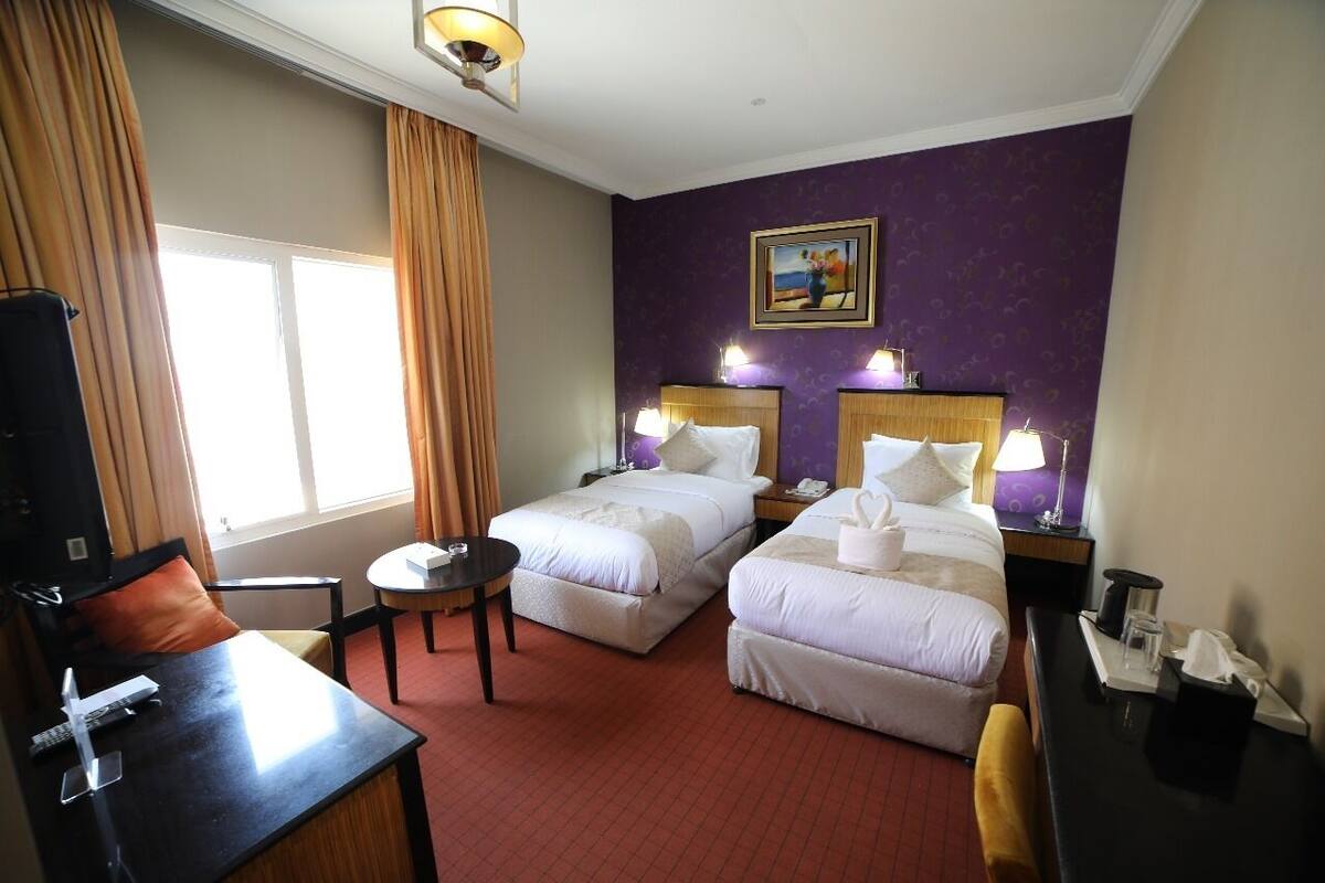 A hotel room with two beds, a desk, a chair, a small table, and a TV.
