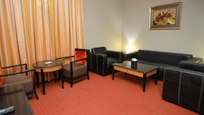 A hotel room with a red carpet, a black leather sofa, a round table, and a chair. - CREEK GATE HOTEL (Sharjah)
