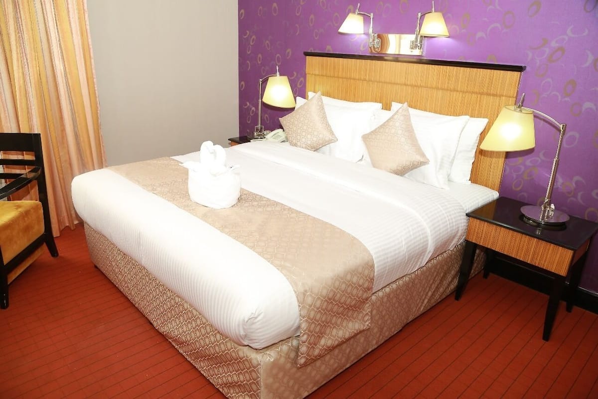 A neatly made bed with a white and beige bedspread, two bedside lamps, and a wooden headboard.