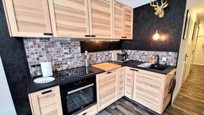 A kitchen with wooden cabinets, a black countertop, a tiled backsplash, and a deer head light fixture. - 100m from ski slopes, 3rd floor, view open, balcony, tv, ski locker, 55m², Valfréjus (Valfréjus)