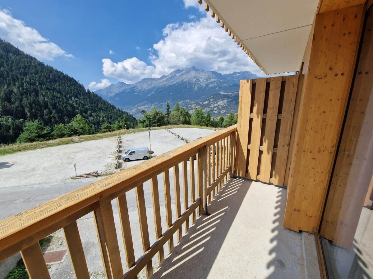 A balcony with a view of a parking area and mountains.