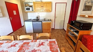 A compact kitchen with wooden cabinets, a microwave, and a sink. There is a dining table with chairs and a red door. - 30m from ski slopes, 5th floor, view open, balcony, tv, ski locker, 55m², Valfréjus (Valfréjus)