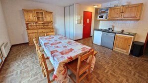 A compact kitchen with wooden cabinets, a dining table with a patterned tablecloth, and a red door. - 30m from ski slopes, 5th floor, view open, balcony, tv, ski locker, 55m², Valfréjus (Valfréjus)