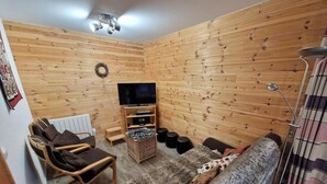 Um quarto acolhedor com paredes de madeira, um sofá, uma poltrona, uma TV e uma pequena mesa.