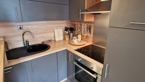 Uma cozinha compacta com armários cinzentos, uma pia preta e um forno de aço inoxidável.