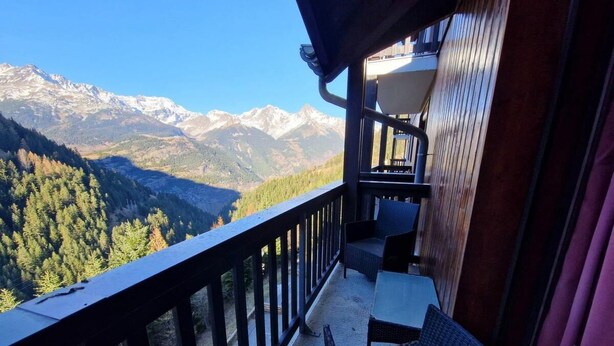 Uma varanda com vista para montanhas nevadas, uma mesa e duas cadeiras.