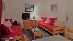 Quarto acolhedor com duas camas de madeira, uma televisão e uma mesa pequena.